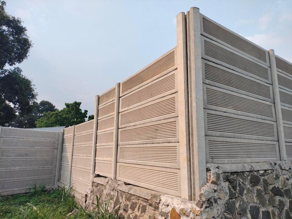 Pagar panel precast motif garis di atas pondasi batu